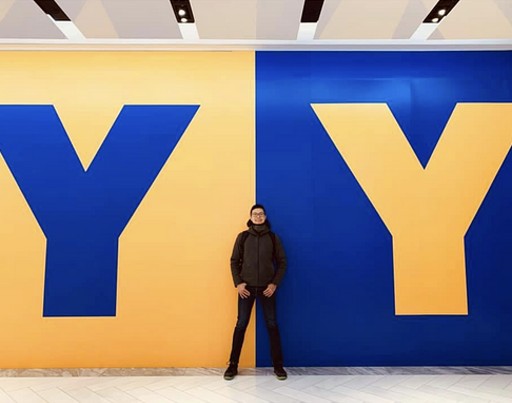 Yuan-Yen Tai standing between two large letter Ys, one blue on yellow and one yellow on blue